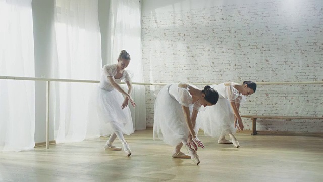 三个年轻和华丽的芭蕾舞者同步跳舞。他们穿着白色的芭蕾舞裙。拍摄于一个阳光明媚的早晨，在一个宽敞明亮的工作室。视频素材