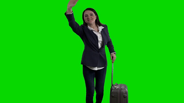 拿着行李的女人对着绿色屏风挥手问好视频下载