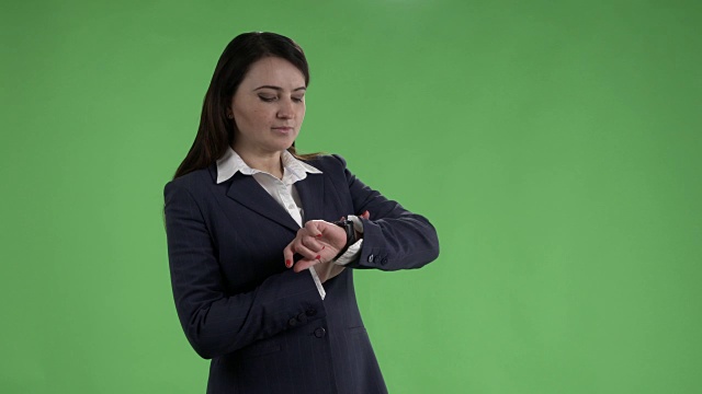等待会议的女人看着手表，对着绿色屏幕挥手问好视频下载