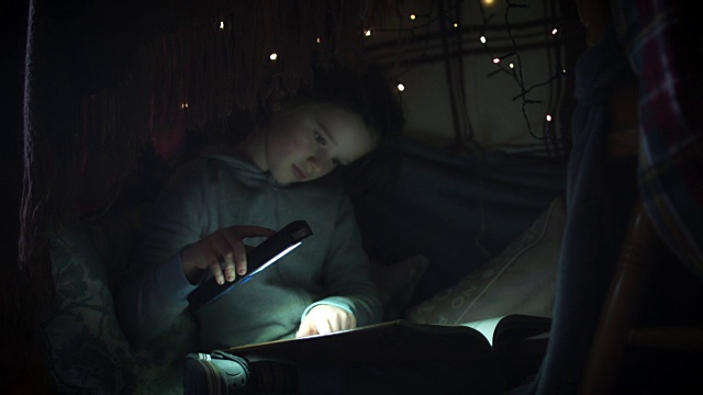 儿童在毯子下用手电筒看书的4k照片视频素材
