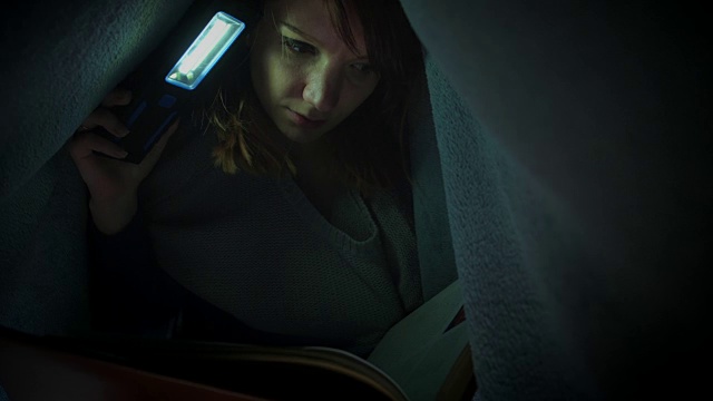 女人在毯子下用手电筒看书的4k照片视频素材