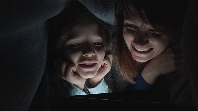 孩子和妈妈在毯子下看平板电脑的4k照片视频素材
