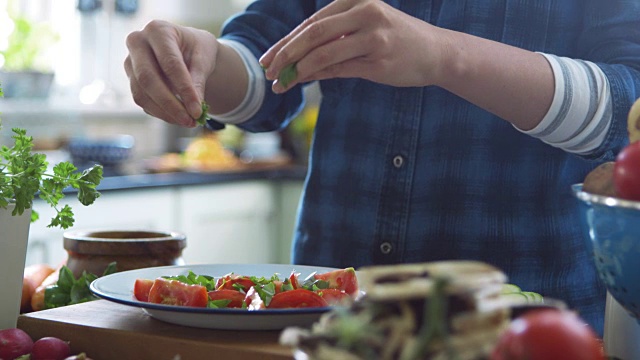一个女人把罗勒叶和橄榄油加在西红柿片上视频素材