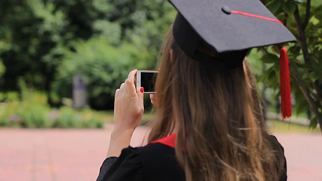 戴着毕业帽的女性在公园用智能手机拍摄朋友视频下载