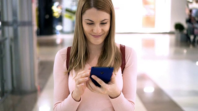 漂亮女人拿着智能手机走在商场里。上网，和朋友交流视频素材