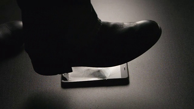 慢镜头:一名男子用一只靴子将智能手机摔在地板上视频素材