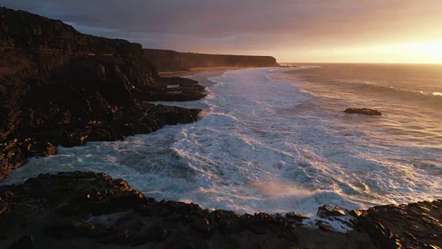 无人机拍摄的日落时海浪撞击岩石的画面视频素材