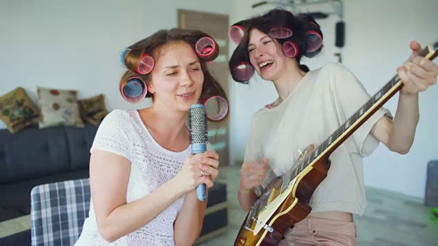 两个有趣的女孩用梳子唱歌，弹电吉他跳舞，唱歌，在家里有快乐视频素材