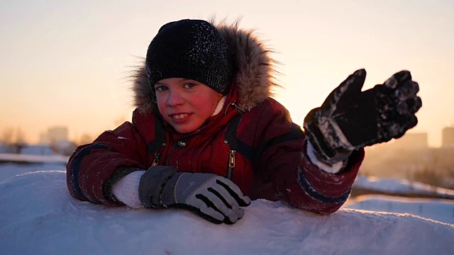 一个孩子在冬日公园挥手，夕阳的背景。雪的冬天的风景。日落时间视频素材