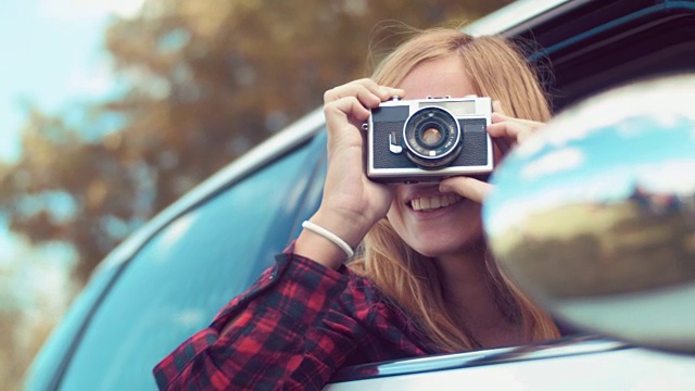手持拍摄的金发女孩从汽车与一个古老的电影相机拍照视频下载
