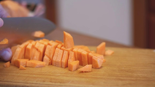 在一个家庭厨房的木制厨房板上用刀切胡萝卜的女人视频下载