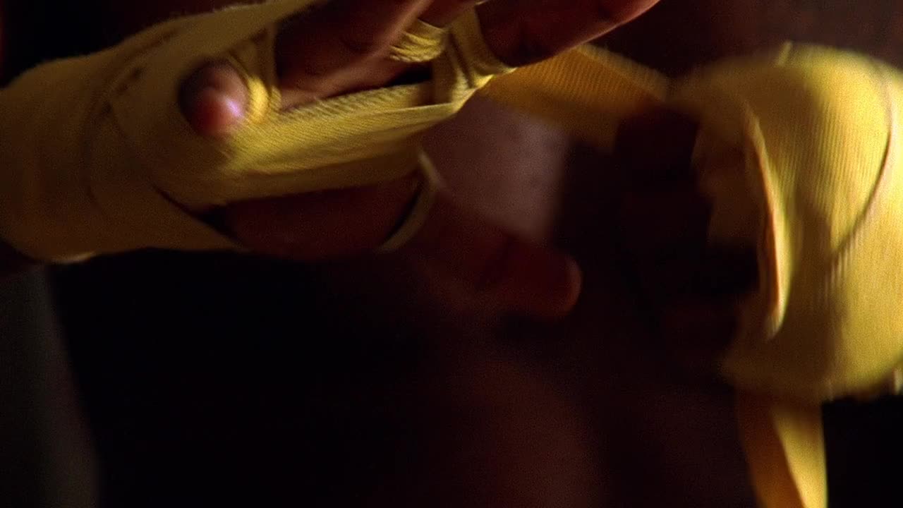 特写镜头向上倾斜放大在更衣室里赤裸的黑人男性拳击手用黄色胶带裹住自己的手视频下载