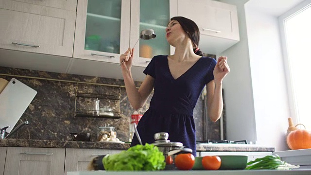 滑稽的妇女家庭主妇在现代厨房做饭时，用大勺煮饭，又唱又跳视频素材