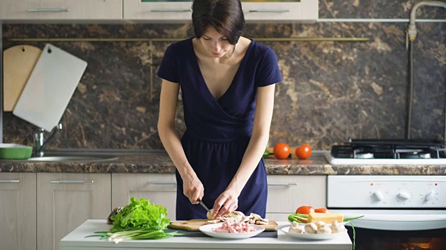 年轻漂亮的女人在家里的厨房里用木板切蘑菇做披萨视频素材