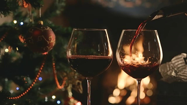 将葡萄酒倒入以圣诞树和壁炉为背景的玻璃杯中视频下载