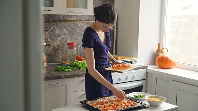 年轻漂亮的女人做饭把西红柿放在比萨饼面团在家里的厨房视频素材