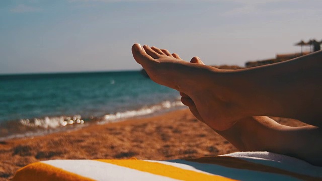 女人的腿躺在海滩太阳躺椅附近的大海视频素材