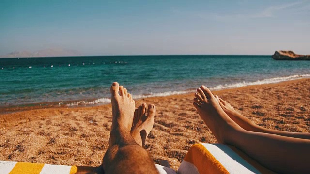 一对夫妇的腿躺在海滩太阳躺椅靠近红海视频素材