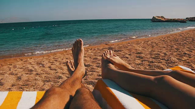 一对夫妇的腿躺在海滩太阳躺椅靠近红海视频素材
