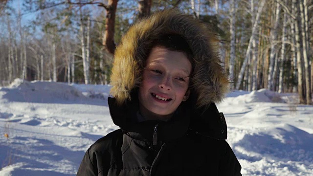 一个十几岁男孩的特写。男孩微笑着，流露出感情。森林里晴朗的冬夜。强烈的风。视频下载