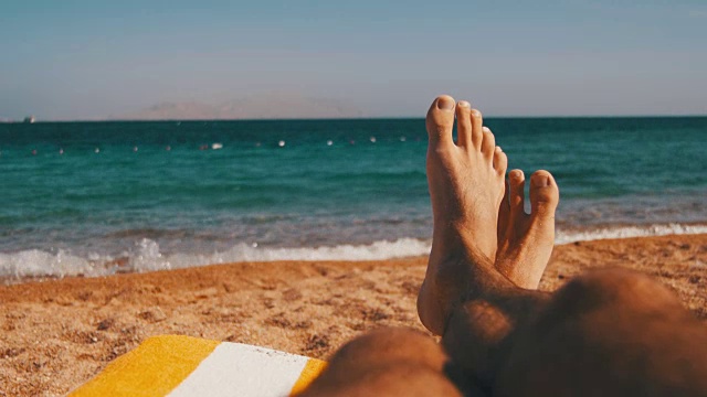 男人的腿躺在海滩太阳躺椅附近的大海视频素材