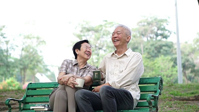 慢镜头快乐的亚洲老夫妇坐在早上的公园喝茶，喝咖啡。交谈并表达爱意视频素材