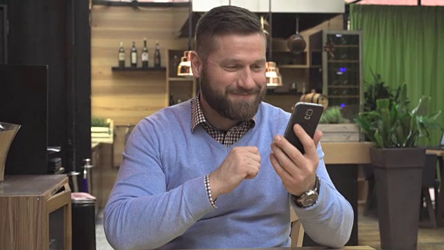 快乐的微笑的男人打视频电话，在酒吧用智能手机skype，稳态摄像头视频素材