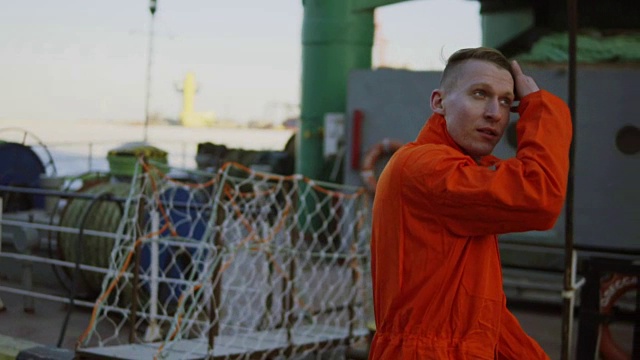 一名身穿橙色制服的年轻工人在休息期间穿过海港。休闲时间视频素材