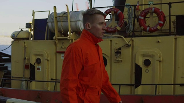 一名身穿橙色制服的年轻工人在休息期间穿过海港。休闲时间视频素材