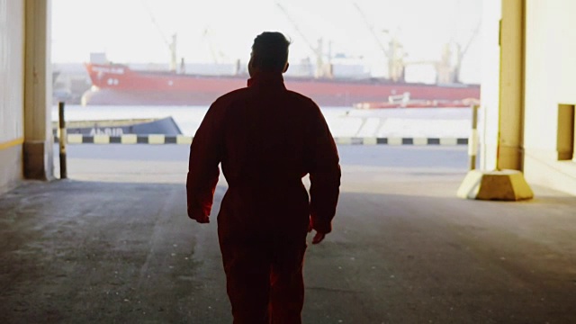 身穿橙色制服的年轻工人在休息期间微笑着穿过海边的港口仓库。Slowmotion视频素材