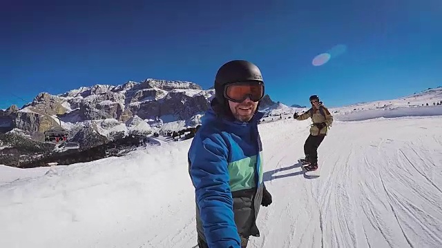 冬天在阿尔卑斯山滑雪。一个男人在滑雪板上滚动，在一个滑雪胜地积雪覆盖的小径上。那家伙在一个极限摄像机前离开了视频素材