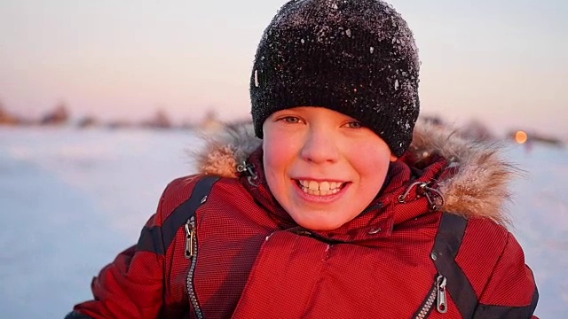 一个孩子在冬天的公园微笑，在夕阳的背景视频下载