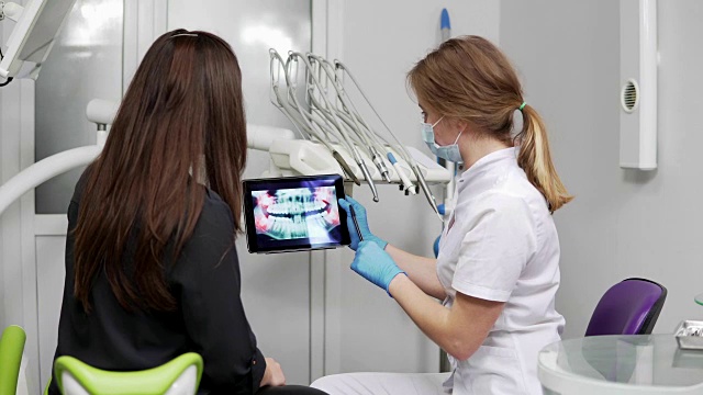女牙医正在给年轻的女病人展示x光片上的牙齿。牙医穿着实验服视频素材