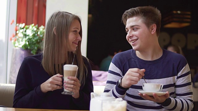 年轻微笑的夫妇在户外咖啡店微笑着喝咖啡。Slowmotion。视频下载