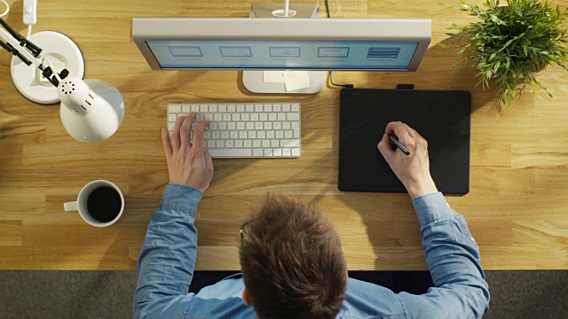 一个年轻的平面设计师在他的桌子上工作的数字绘图平板电脑的俯视图。视频素材