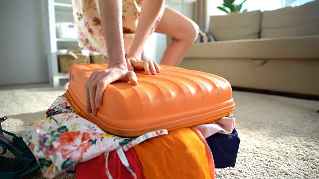 一个年轻女子正试图合上一个满满的橙色行李箱。时间流逝视频素材