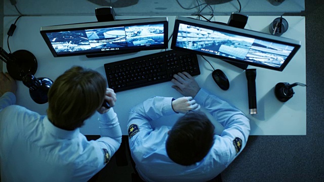一个保安和他的显示器的顶视图看着监视器与视频监控录像和谈话对讲机。他上夜班。视频下载