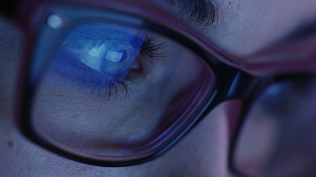 近距离拍摄的女人眼睛在眼镜盯着一个工作平板电脑屏幕在黑暗。视频素材