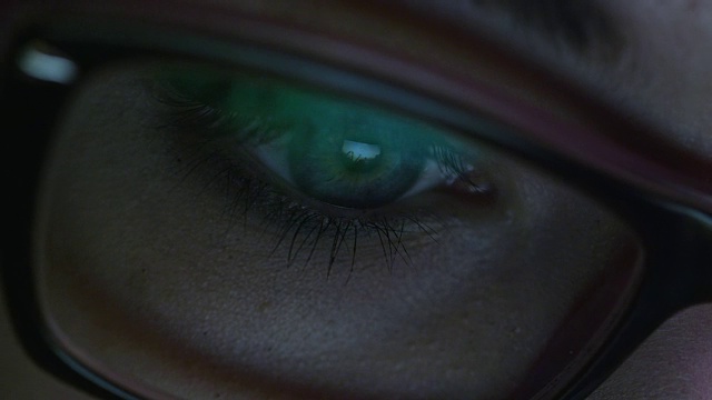 近距离拍摄的女人眼睛在眼镜盯着一个工作的电脑屏幕在黑暗。视频素材