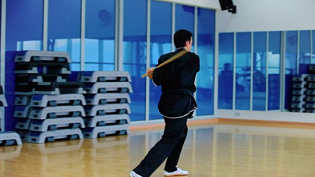 身穿黑色服装的男子在体育馆里用棍棒与隐形对手搏斗视频下载