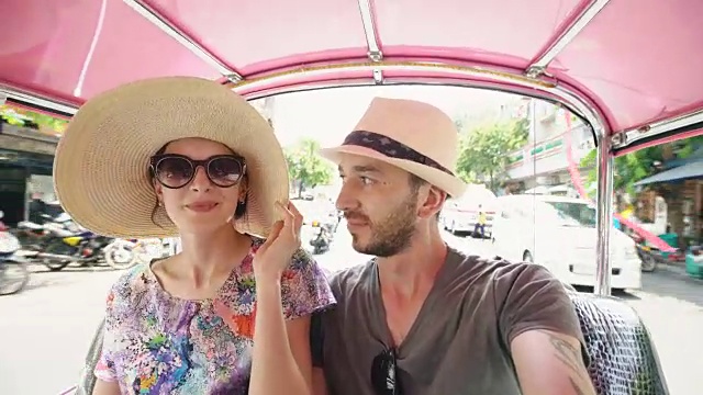 年轻英俊的男子戴着帽子，他的女朋友乘坐泰国传统巴士颂泰。一对夫妇在泰国度蜜月视频素材