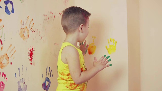 快乐可爱的小男孩在墙上留下五颜六色的手印玩得很开心。年轻的幸福的家庭。母亲和孩子的概念。Slowmotion视频下载