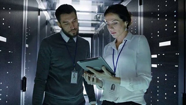 两位IT工程师走进数据中心/服务器室，交谈，用平板电脑运行诊断。视频素材