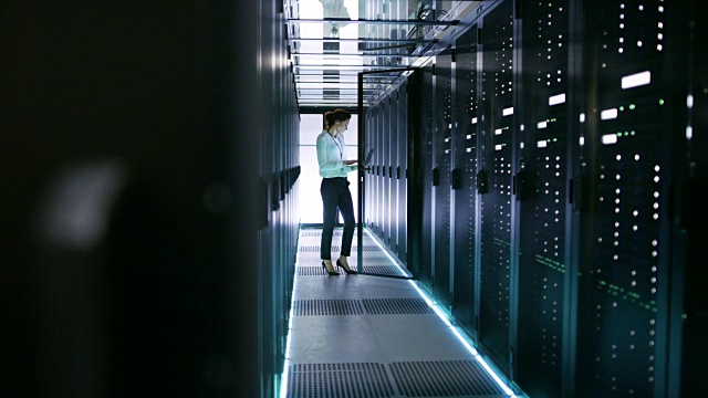 数据中心的女服务器工程师用她的笔记本电脑在机架服务器上工作。视频素材