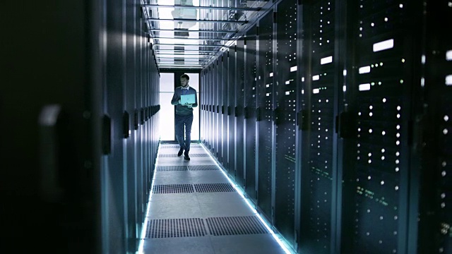 男性服务器工程师带着笔记本电脑走过堆满机架服务器的工作数据中心。视频素材