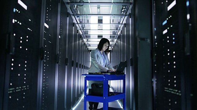 亚洲女IT工程师在一个大型数据中心满是机架服务器的应急手推车笔记本上工作。视频素材