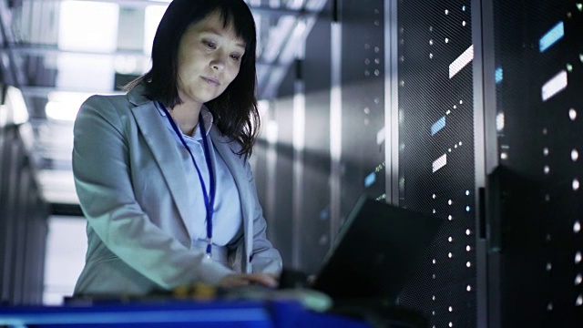 亚洲女性IT工程师工作在一个应急车笔记本电脑，她扫描硬盘。她在满是机架服务器的大数据中心。视频素材