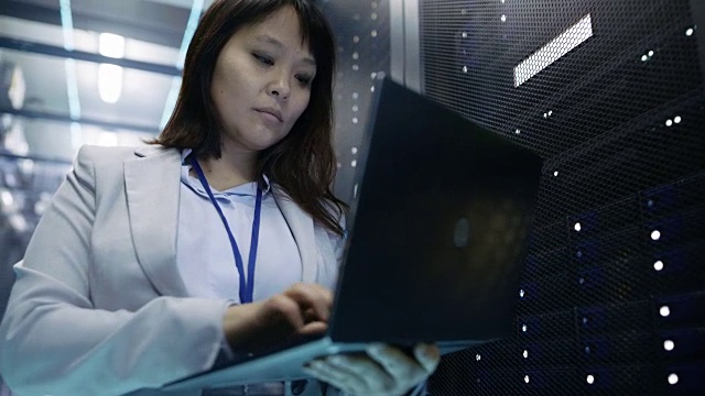 特写的女性亚洲IT工程师工作在一个笔记本电脑上的数据中心充满机架服务器。视频素材