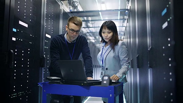 高加索男性和亚洲女性服务器工程师与碰撞车笔记本电脑在大数据中心满机架服务器。视频素材