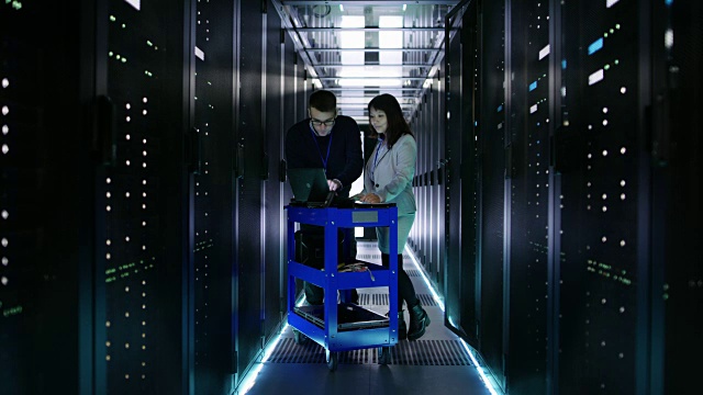 高加索男性和亚洲女性服务器工程师与碰撞车笔记本电脑在大数据中心满机架服务器。视频素材